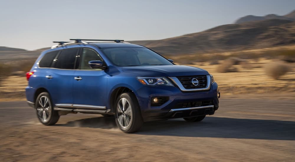 A blue 2017 Nissan Pathfinder is shown driving off-road in a desert.
