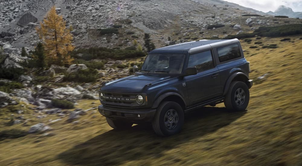 A dark blue 2021 Ford Bronco is shown driving off-road downhill.