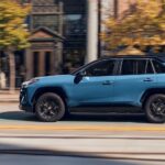 A blue 2023 Toyota RAV4 Hybrid Woodland is shown driving to view a Toyota RAV4 for sale.
