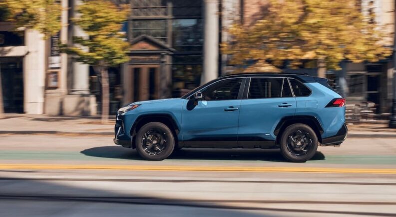 A blue 2023 Toyota RAV4 Hybrid Woodland is shown driving to view a Toyota RAV4 for sale.