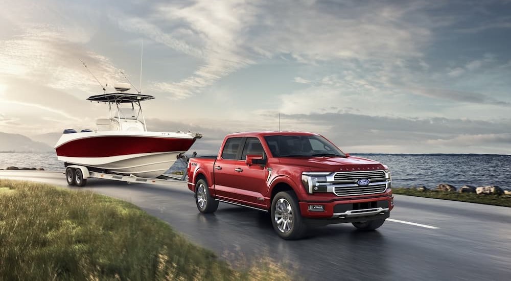 A red 2024 Ford F-150 Platinum is shown towing a boat near an ocean.