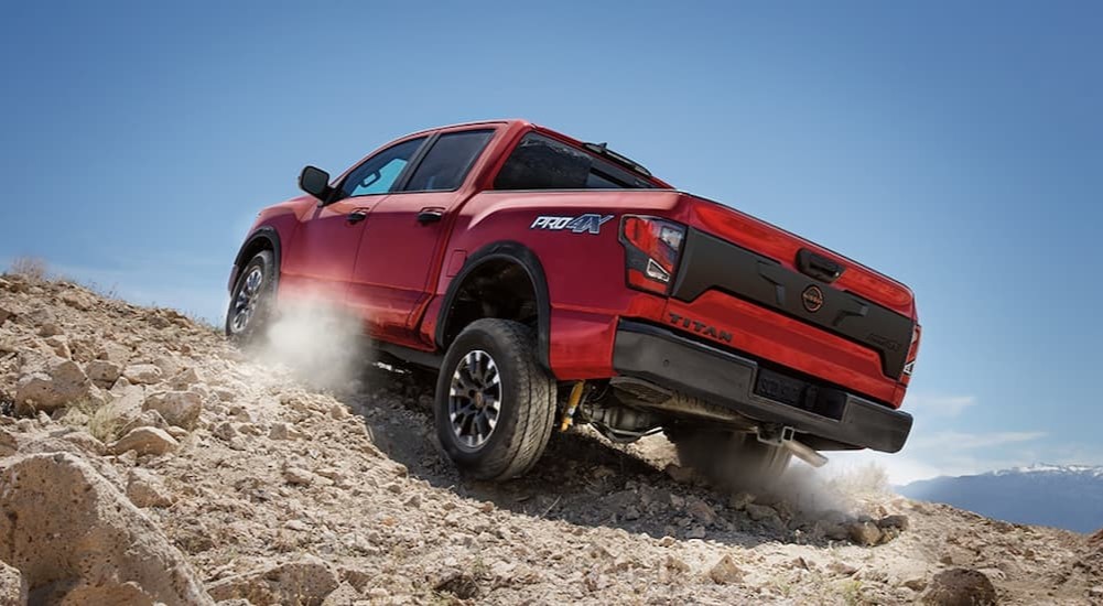 A red 2024 Nissan Titan PRO-4X is shown driving on a rocky hill.