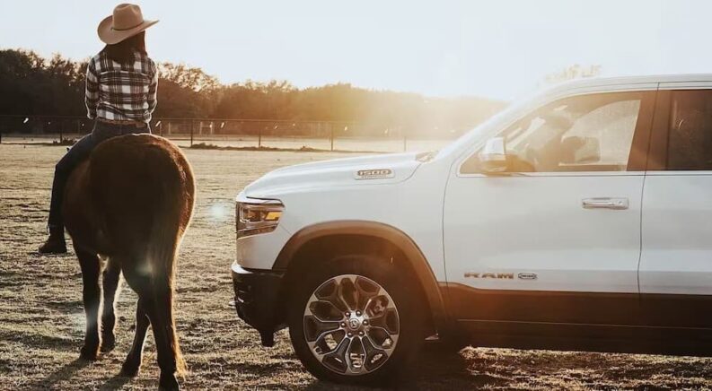 A white 2024 Ram 1500 is shown parked next to a horse after visiting a used RAM dealership.