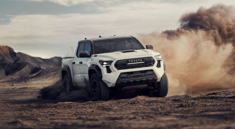 A white 2024 Toyota Tacoma for sale is shown driving off-road in a desert.