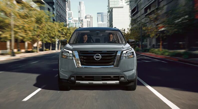 A grey 2024 Nissan Pathfinder is shown from a front view driving down a city boulevard.