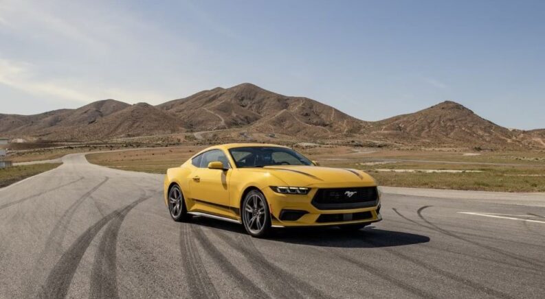 A yellow 2024 Ford Mustang is shown near mountains after visiting local Ford dealers.