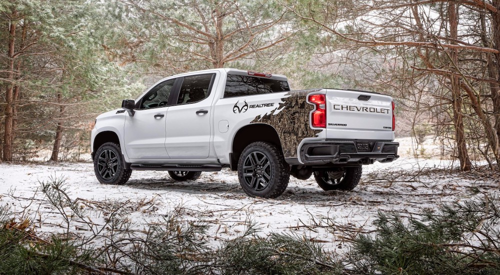 A white 2021 Chevrolet Silverado Realtree Edition is shown parked in a forest as seen from behind.