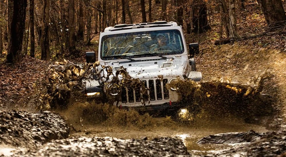 A white 2021 Jeep Wrangler Rubicon is shown driving on a muddy trail after visiting a Jeep dealer.