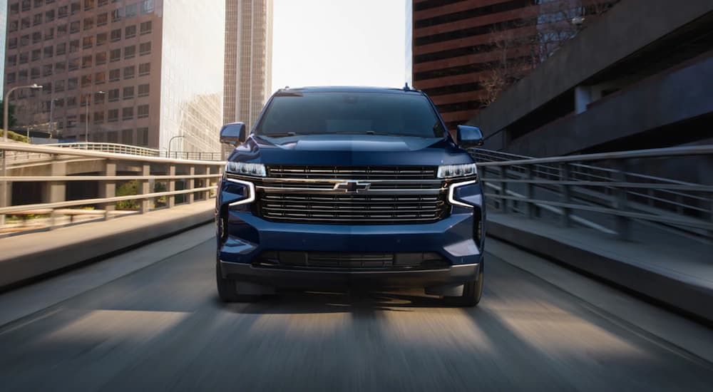 A blue 2023 Chevy Tahoe is shown driving in a city.