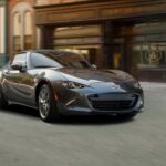 A gray 2023 Mazda Miata RF is shown driving to a used sports car dealer.