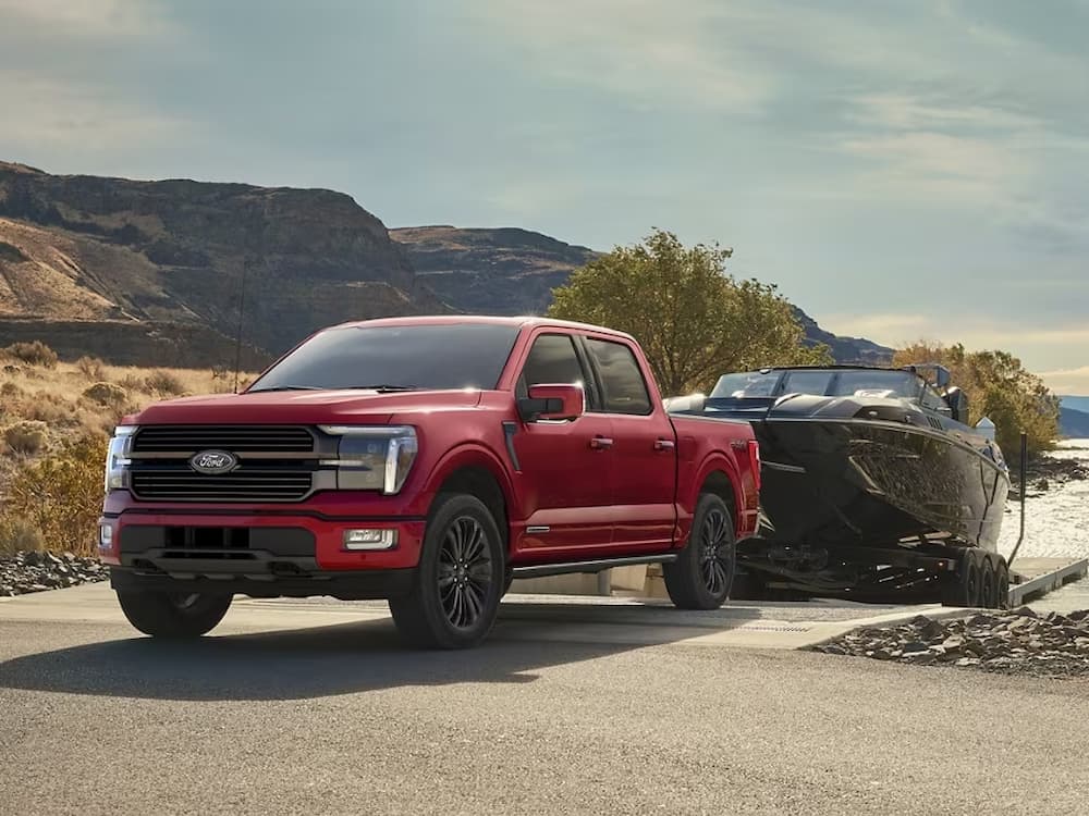 A red 2024 Ford F-150 is shown towing a black boat.