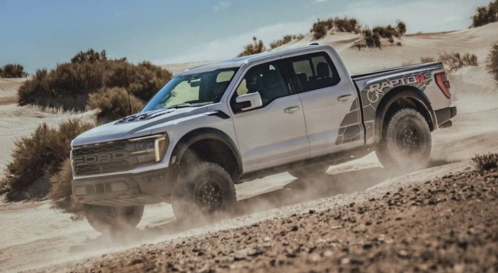 A white 2024 Ford F-150 Raptor is shown driving off-road.