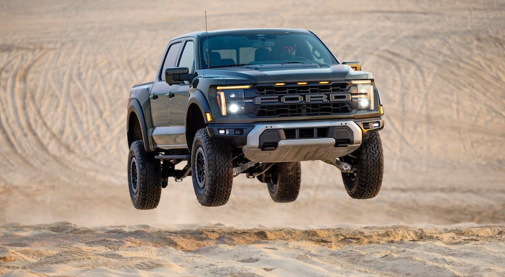 A green 2024 Ford F-150 Raptor is shown off-roading in a desert.