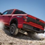 A red 2024 Nissan Titan PRO-4X is shown driving off-road after visiting a Nissan Titan for sale.