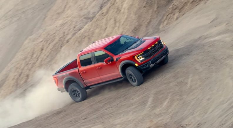 A red 2021 used Ford F-150 Raptor for sale is shown kicking up dust.