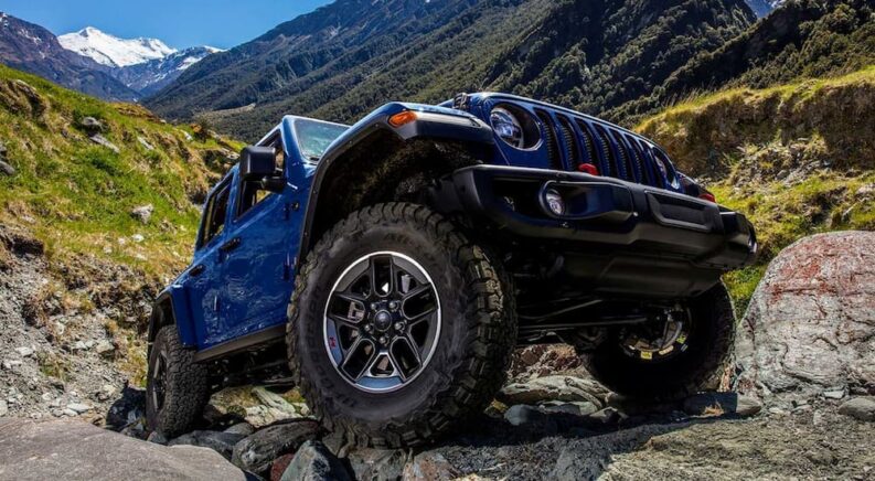 A blue 2019 Jeep Wrangler Rubicon is shown driving off-road in a valley after visiting a Jeep dealer.