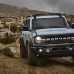 One of the more popular used SUVs for sale, a blue 2021 Ford Bronco, is shown driving off-road.