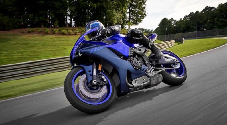 A blue 2023 Yamaha YZF-R1 is shown racing on a racetrack.