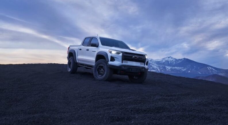 A white 2024 Chevy Colorado ZR2 Bison is shown parked near a mountain after visiting a used truck dealer.