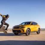 A skateboarder is shown riding a skateboard near a yellow 2024 Dodge Hornet for sale.