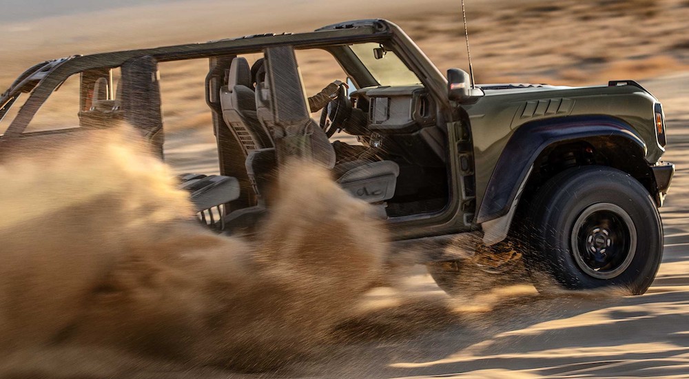 A dark green 2024 Ford Bronco Raptor is shown driving off-road in a desert.