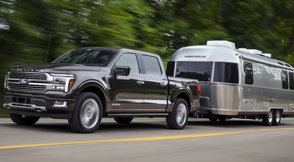 A dark gray 2024 Ford F-150 is shown towing a trailer on a highway.