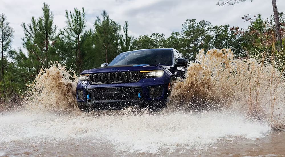 A dark blue 2024 Jeep Grand Cherokee 4xe splashes through deep water while overlanding.
