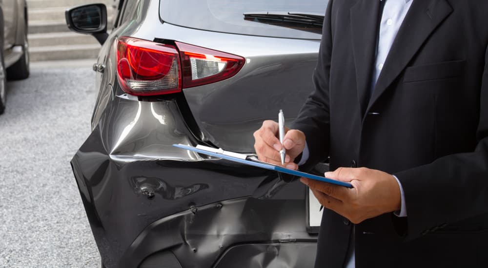 A man is shown writing an insurance claim near a damaged car.