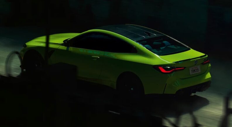 A neon green 2024 BMW M4 Coupe, barely illuminated in a dark tunnel.