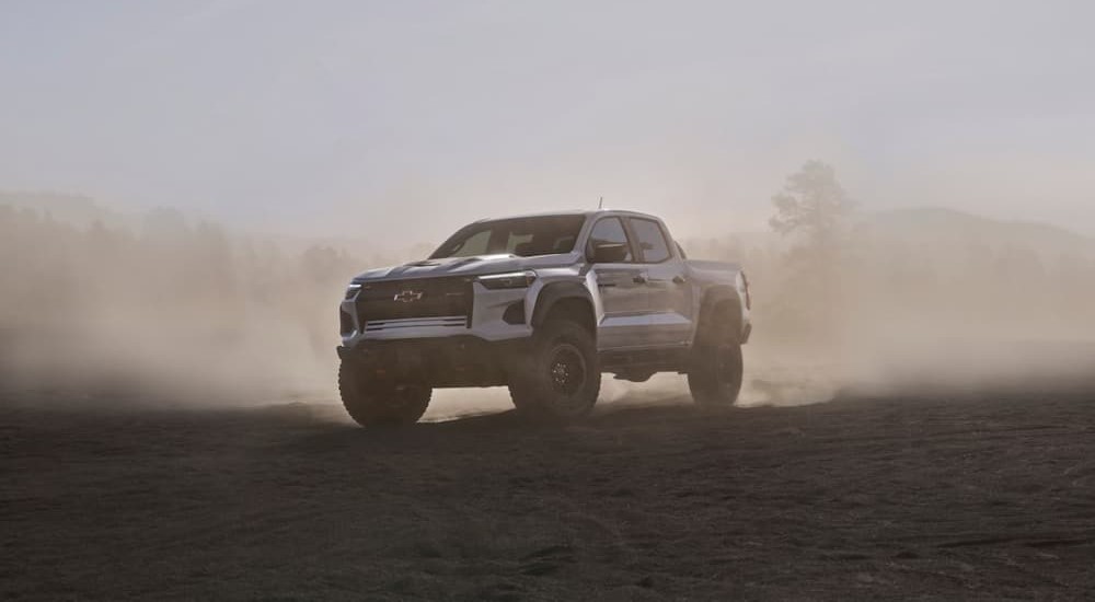 A white 2024 Chevy Colorado ZR2 Bison is shown driving in a dust cloud.