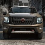 A brown 2024 Nissan Titan PRO-4X is shown parked near a Nissan dealer.