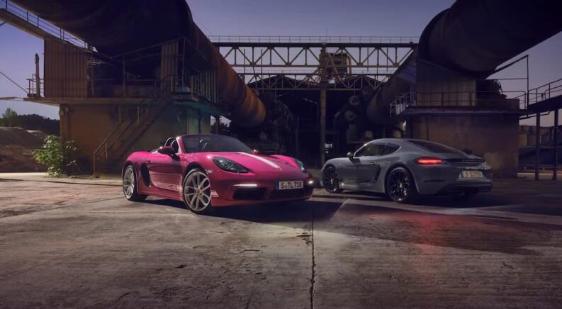A pink 2024 Porsche 718 Boxter and grey 2024 Porsche 718 Cayman parked at an industrial site.