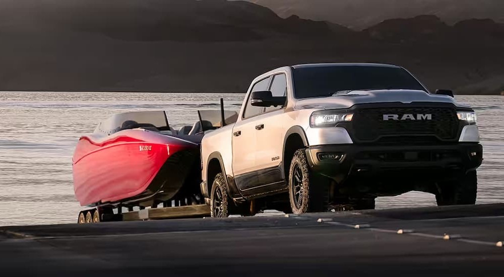 A silver 2025 Ram 1500 towing a motorboat out of a body of water.