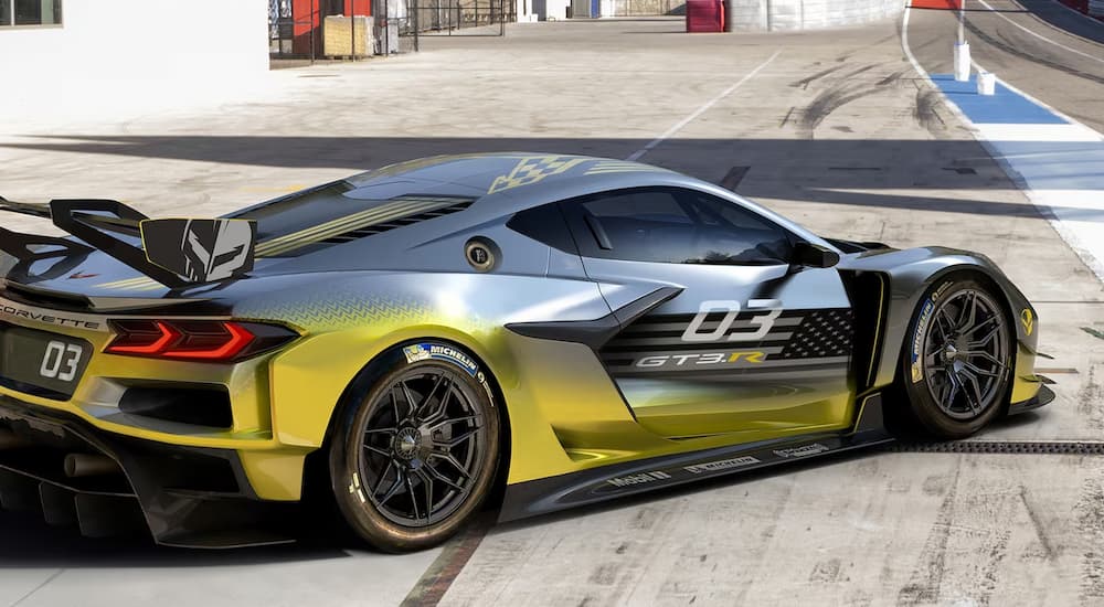 A grey and yellow Chevy Corvette Z06 GT3.R parked at an angle on a racetrack near a Chevy dealer.