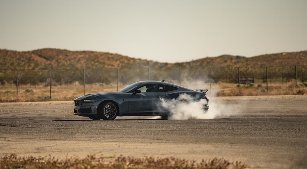 A grey 2024 Ford Mustang Dark Horse doing a burnout in an empty lot.