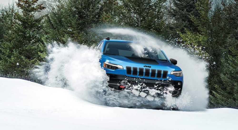 A blue 2023 Jeep Cherokee Trailhawk barrels through deep snow.