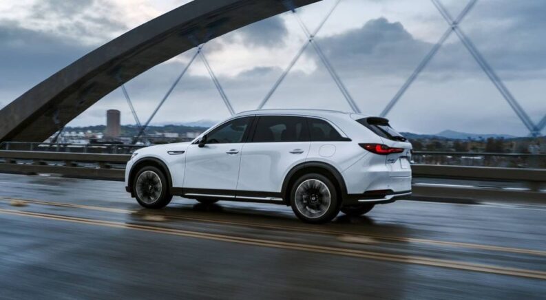 Side view of a white 2024 Mazda CX-90 driving over a modern bridge.
