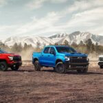 Three 2024 Chevy Silverado 1500s of varying trim levels parked in front of mountains.