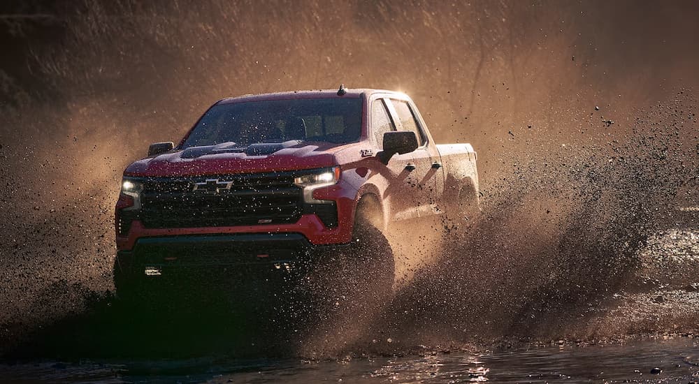 A red 2024 Chevy Silverado 1500 LT Trail Boss kicking up mud while off-roading.