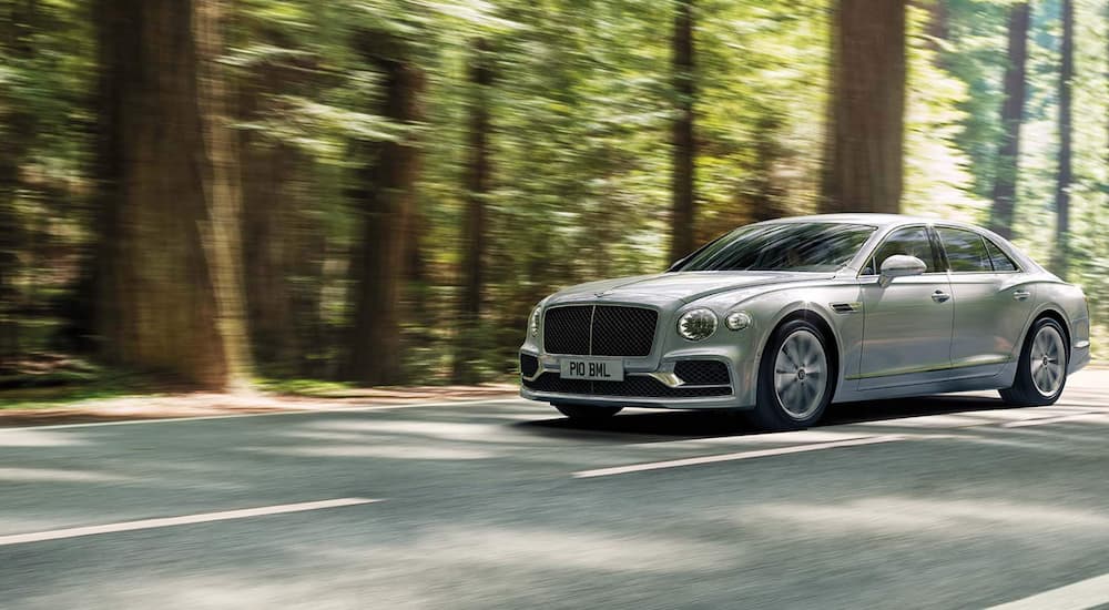 A silver third-generation Bentley Flying Spur driving on a wooded road.