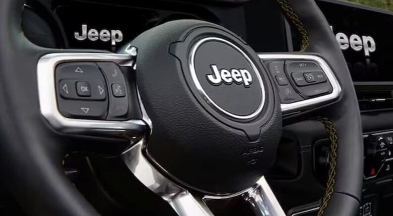 A close-up on the steering wheel in a 2024 Jeep Wrangler is shown at a Jeep dealer.