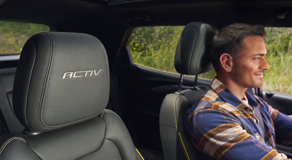 A person is shown sitting in the black interior of a 2024 Chevy Trailblazer ACTIV.