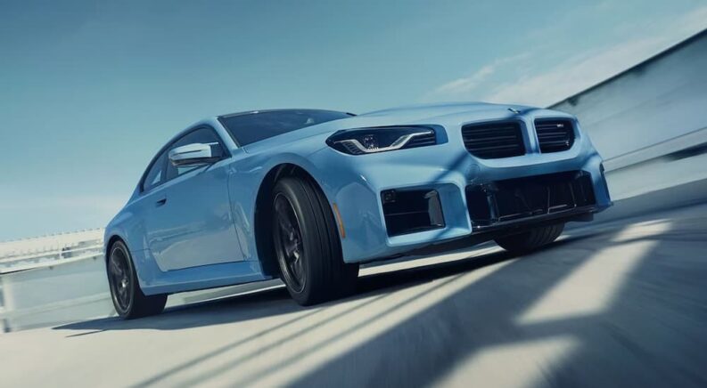 A blue 2024 BMW M2 Coupe is shown driving from a BMW M certified dealer.