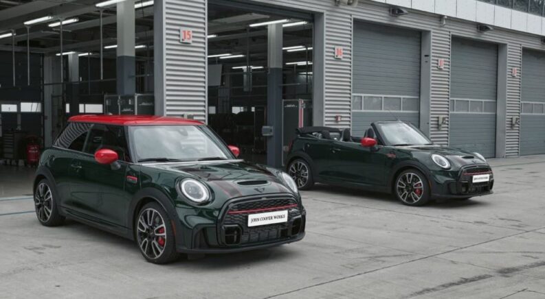 A green hardtop and green convertible 2024 MINI John Cooper Works are shown in front of open garage bays.