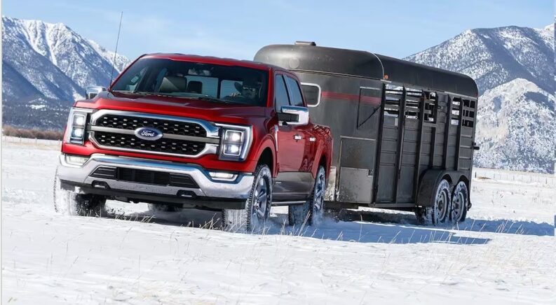 A red 2024 Ford F-150 towing a trailer over a snowy field.