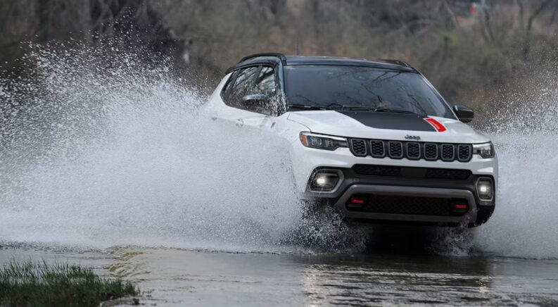 A white 2024 Jeep Compass Trailhawk splashing through water while off-roading.