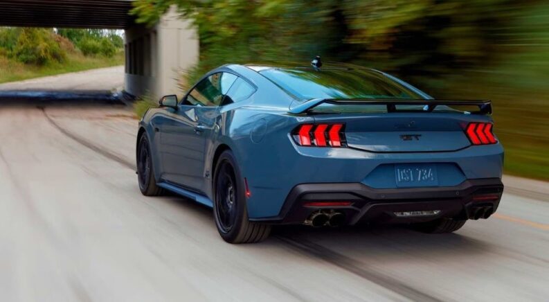 A blue 2024 Ford Mustang GT is shown driving to visit a Ford dealer.