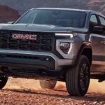 A silver 2024 GMC Canyon Elevation is shown driving on a rocky dirt road.
