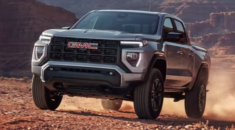 A silver 2024 GMC Canyon Elevation is shown driving on a rocky dirt road.