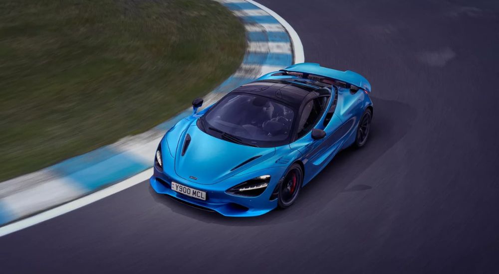 A blue 2024 McLaren 750S is shown from a high angle rounding a corner.